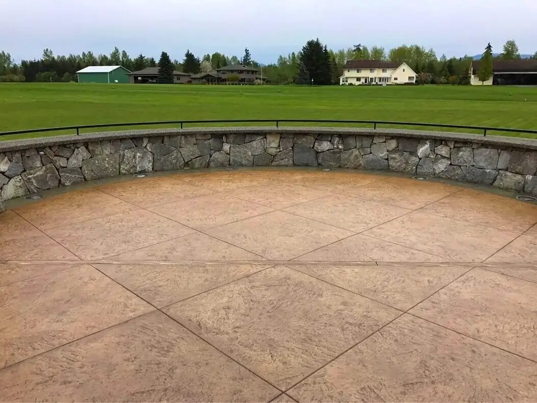 Curved seating area with a stamped concrete floor in a diamond pattern, bordered by a stone retaining wall.