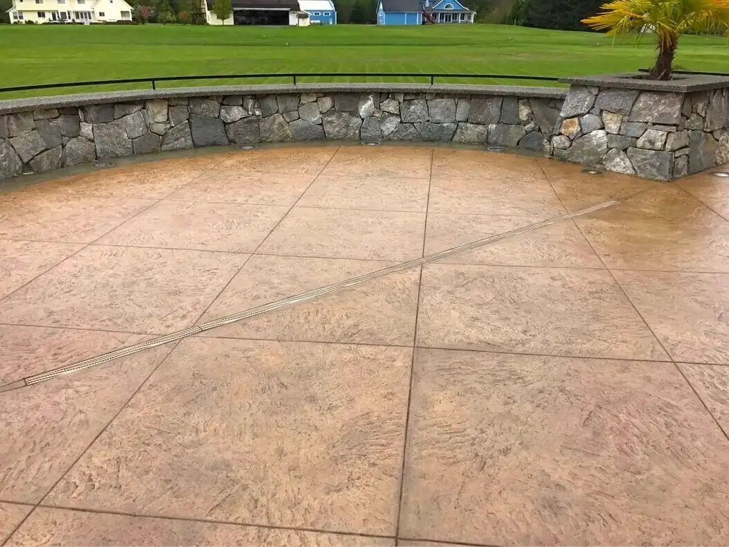 Stamped concrete patio with a linear channel drain and integrated lighting next to a curved stone wall.