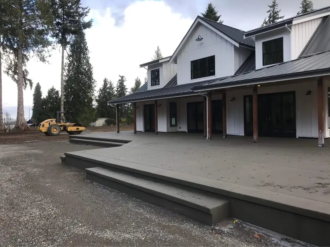 Angled perspective of a large, dark gray concrete patio with two tiers of steps in Bellevue, WA, next to a farmhouse.