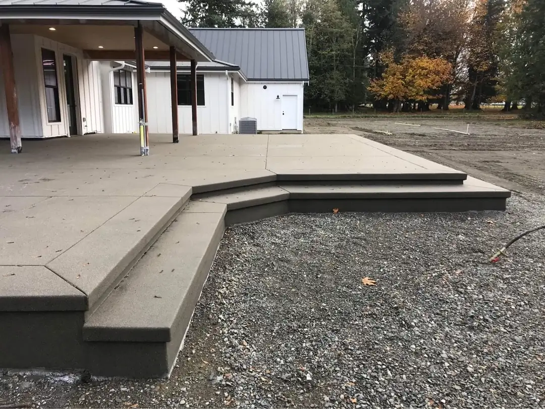 View across the geometric concrete patio, highlighting the integrated steps and the uniform dark gray sand finish.