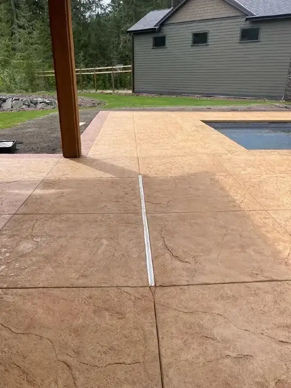 A linear channel drain installed at the edge of the stamped concrete patio for effective water management.