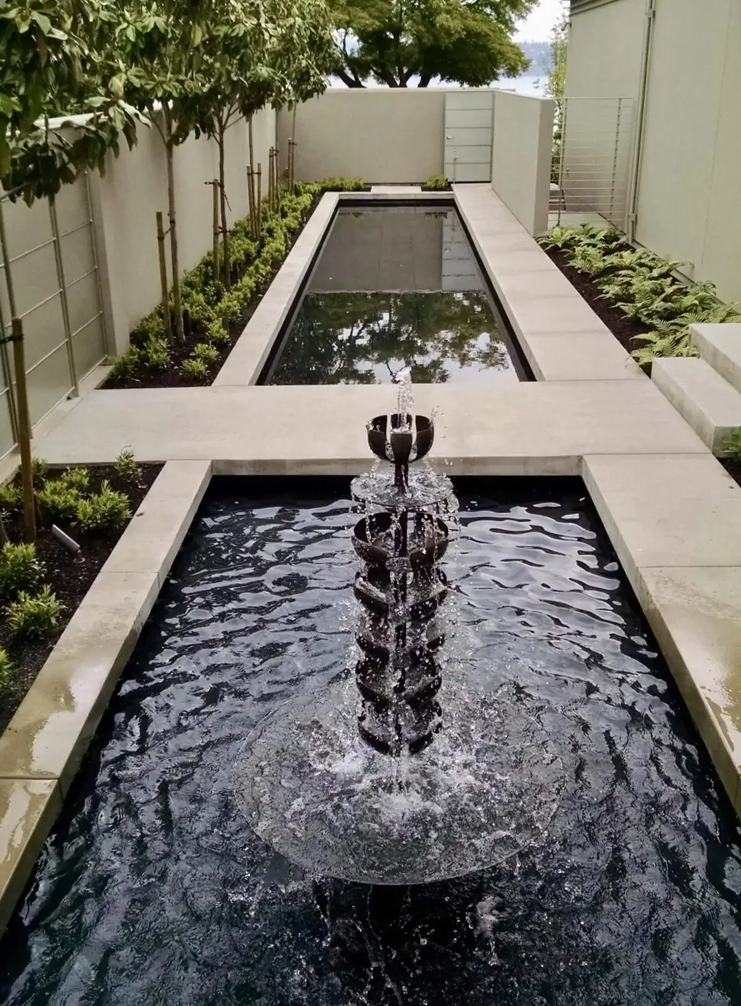 Long view of a custom concrete water feature with a fountain in a modern Bellevue landscape project.