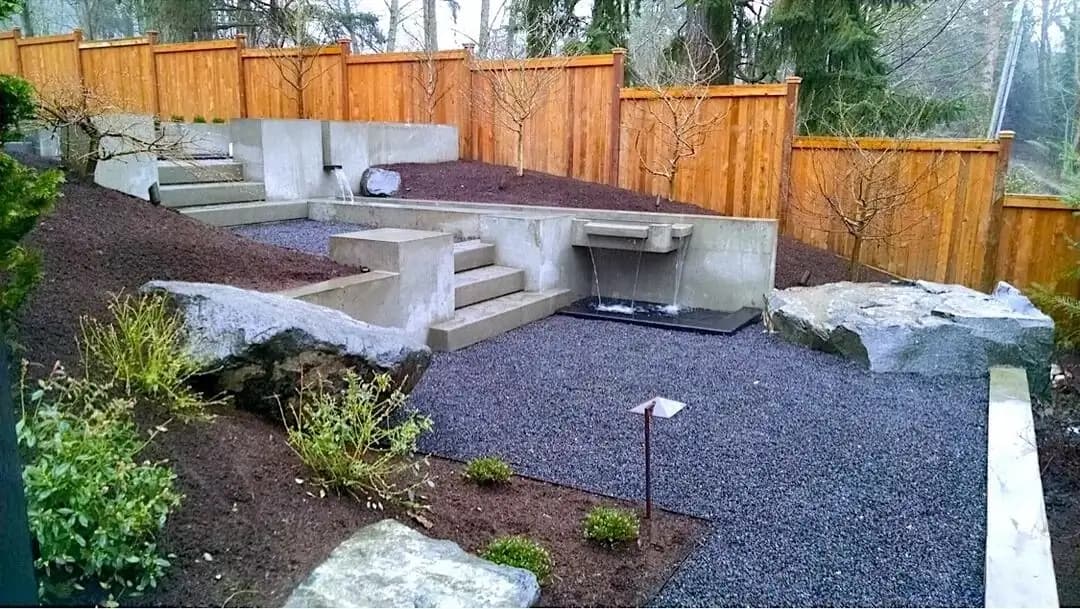 Multi-level concrete retaining walls and steps with an integrated waterfall feature in a Bellevue backyard.