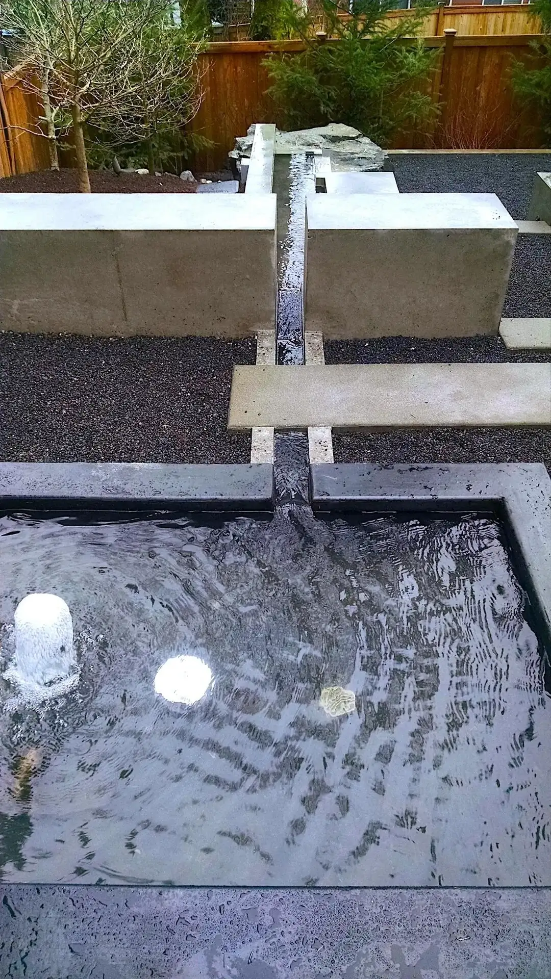Close-up of the smooth concrete water channel spilling into a lower basin with integrated lighting.