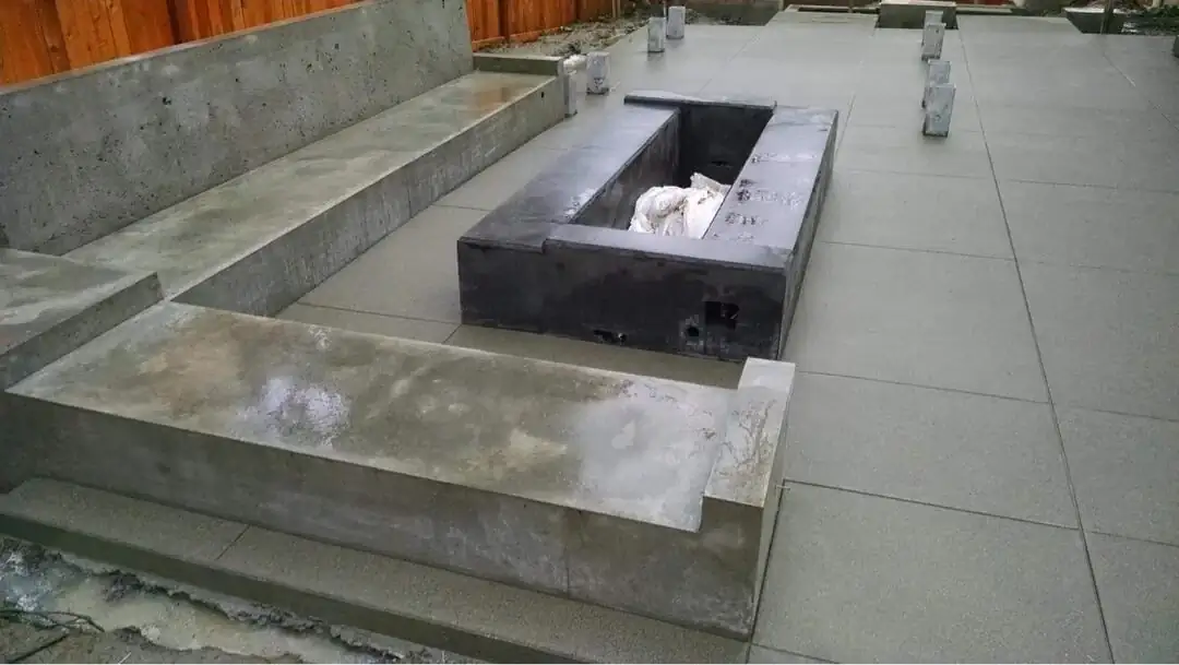 A newly poured dark concrete fire pit and integrated L-shaped seat wall on a saw-cut patio.