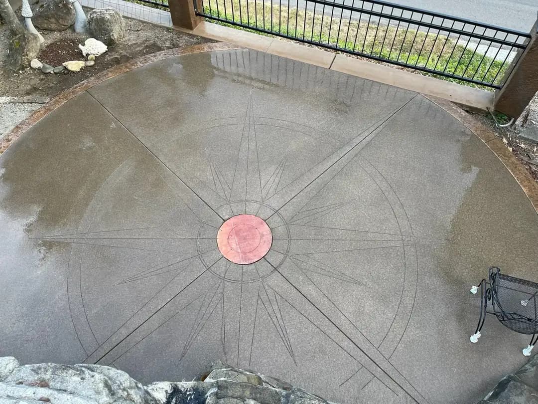 Close-up of the saw-cut compass rose detail on the sand-finish concrete patio in Puyallup, with a red center.