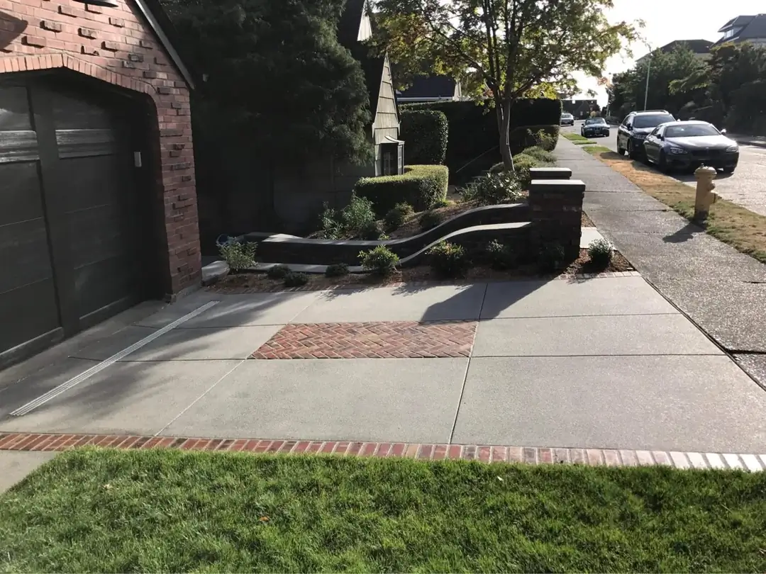 Wide view of a new concrete driveway in Tacoma featuring a channel drain and a stamped brick inlay at the garage.