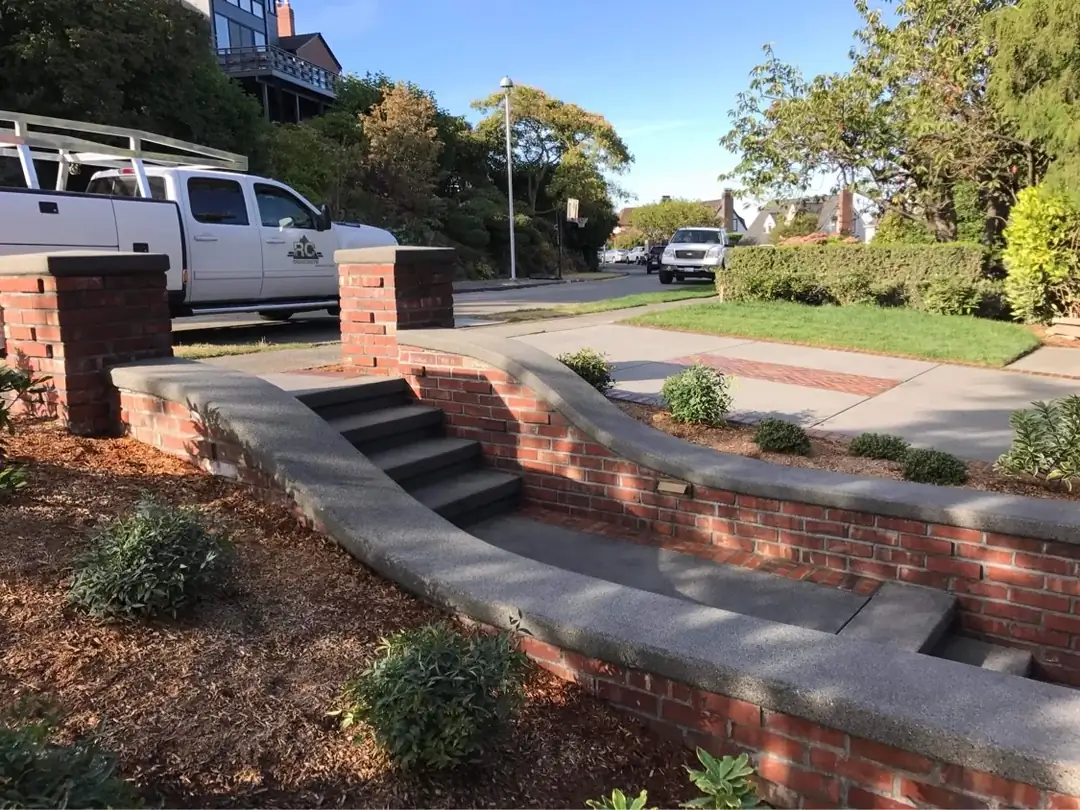 Curved brick retaining wall with dark concrete caps and integrated steps leading down to a public sidewalk.