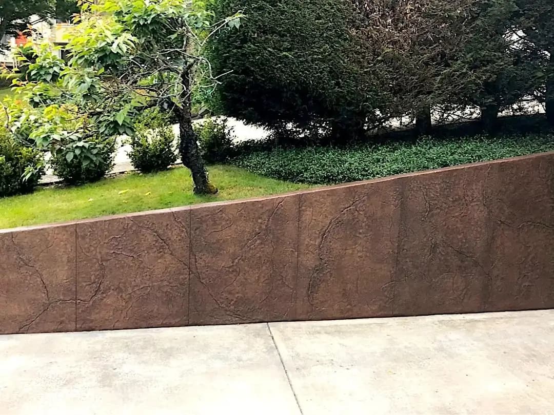 Sloped stamped concrete retaining wall in a brown random stone pattern next to a driveway in Tacoma.