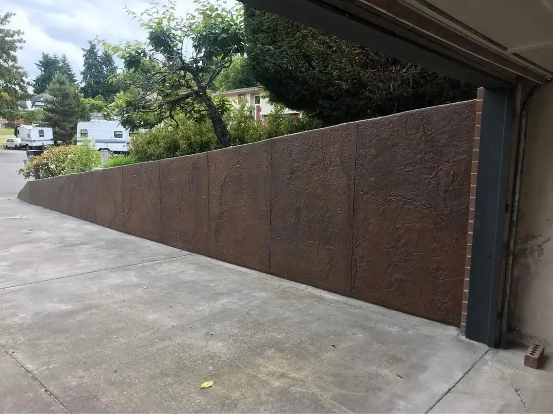 Stamped concrete retaining wall terminating at a garage entrance, showing the slope and texture.