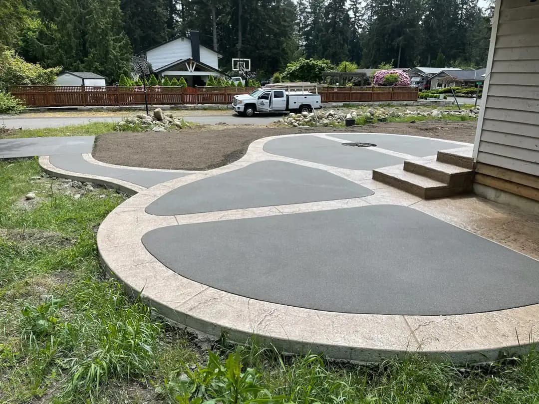 Angled view of a new concrete patio in Puyallup, highlighting the stamped border and contrasting dark gray panels.