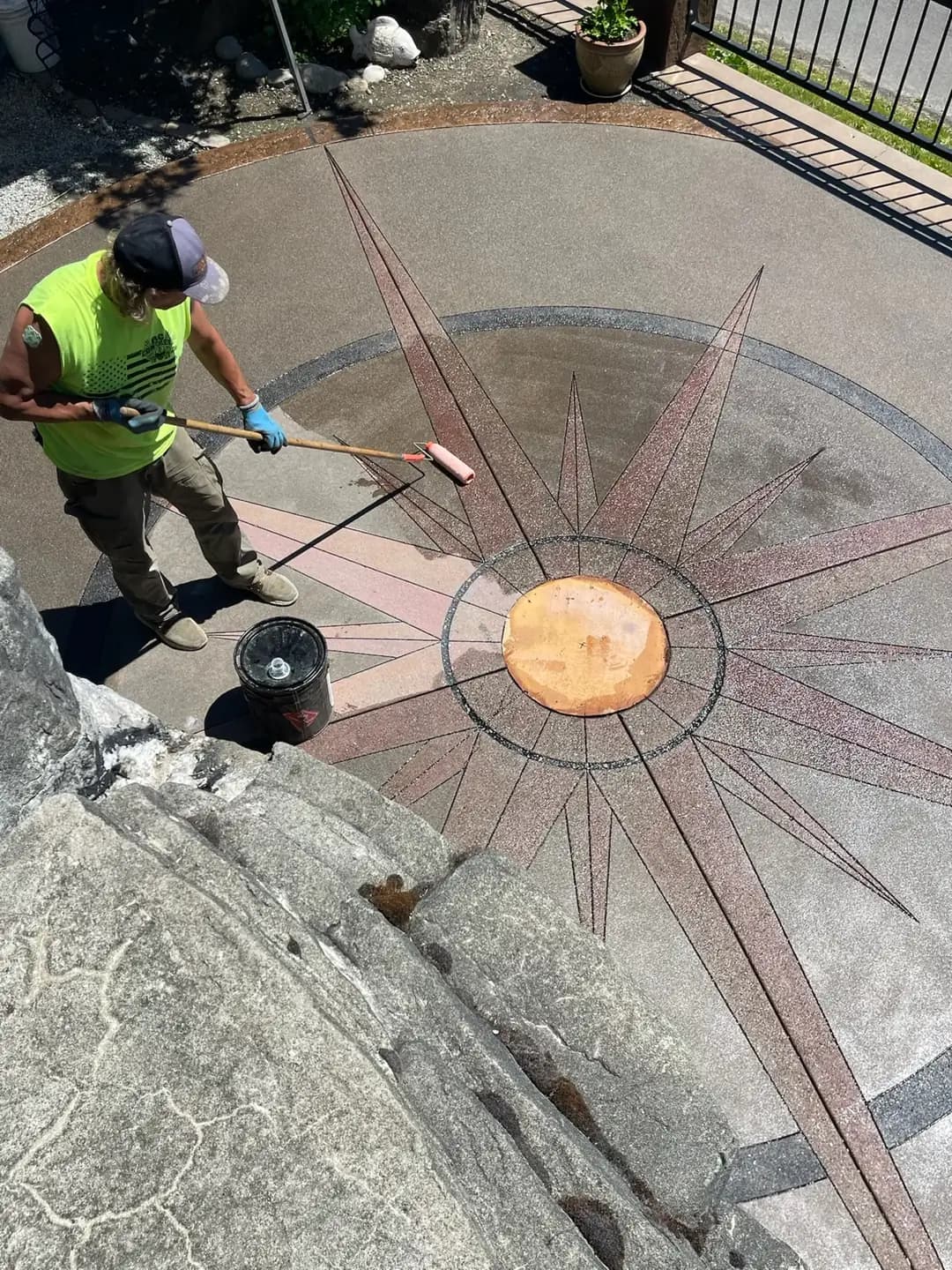 Craftsman applying sealer with a roller to the exposed aggregate compass design on a new patio in Puyallup.