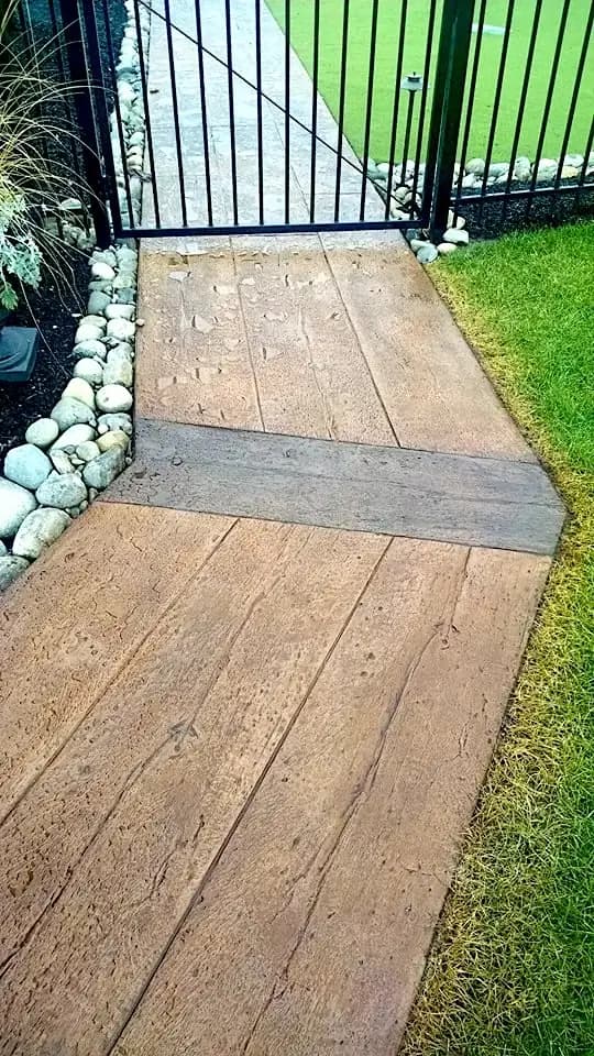 A close-up of the stamped concrete walkway in Bellevue where it meets a metal gate, showing the two-tone effect.
