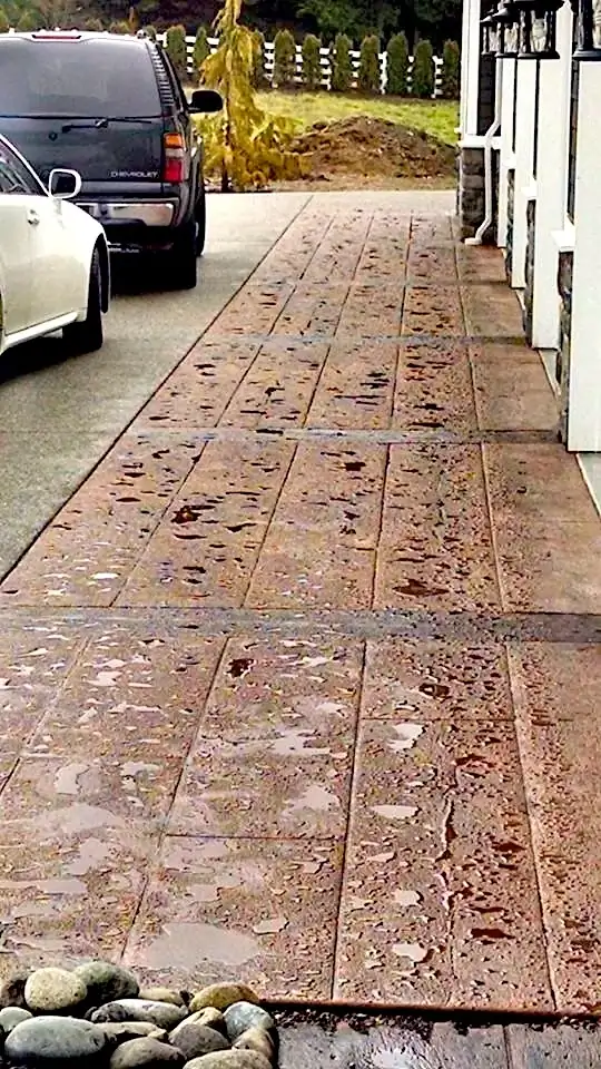 Side view of the wood plank stamped concrete path running alongside the house, wet from recent rain.