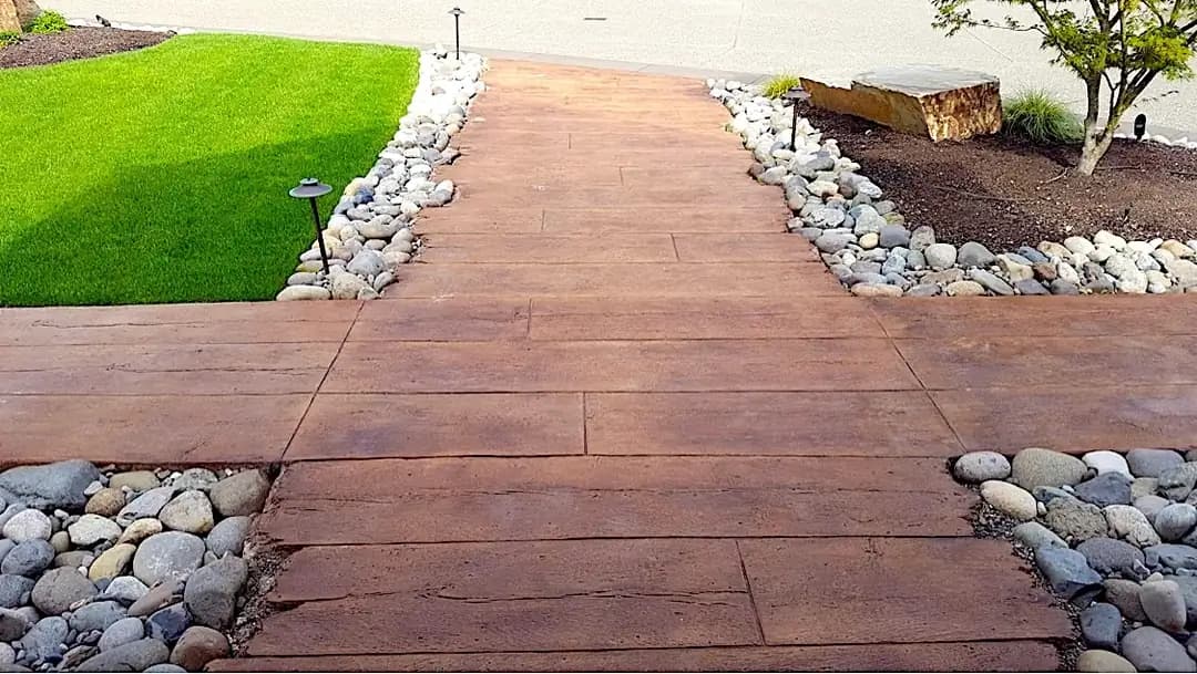 A long view of the wood plank stamped concrete walkway, bordered by river rocks and landscape lighting.