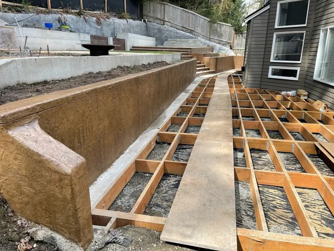 Textured stamped concrete retaining wall in Bellevue adjacent to framing for a new wood deck installation.