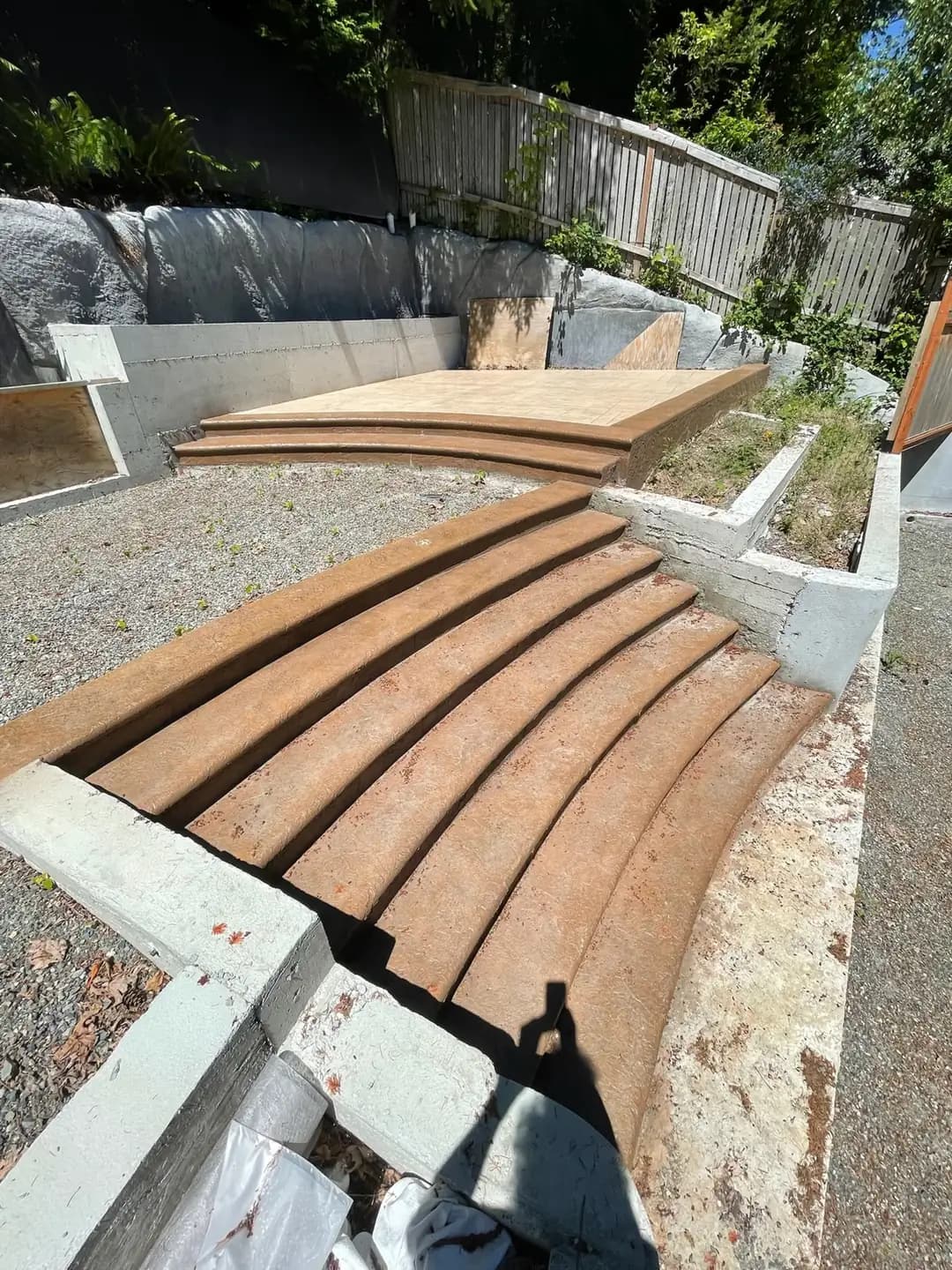 Wide, curved concrete steps with a dark brown finish leading to an upper landing, set against a gravel base.