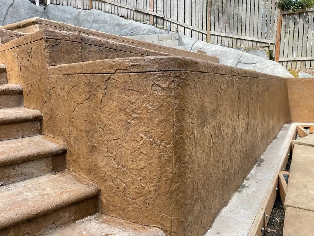 Corner detail of a stamped concrete seat wall and steps, showing a seamless, heavy stone texture finish.