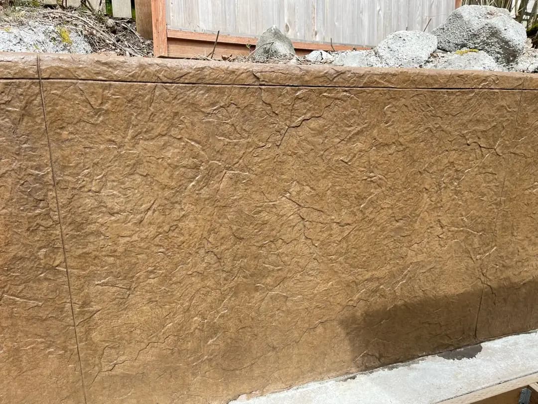 Close-up of a vertical concrete surface with a stamped seamless stone texture and a dark brown stain.