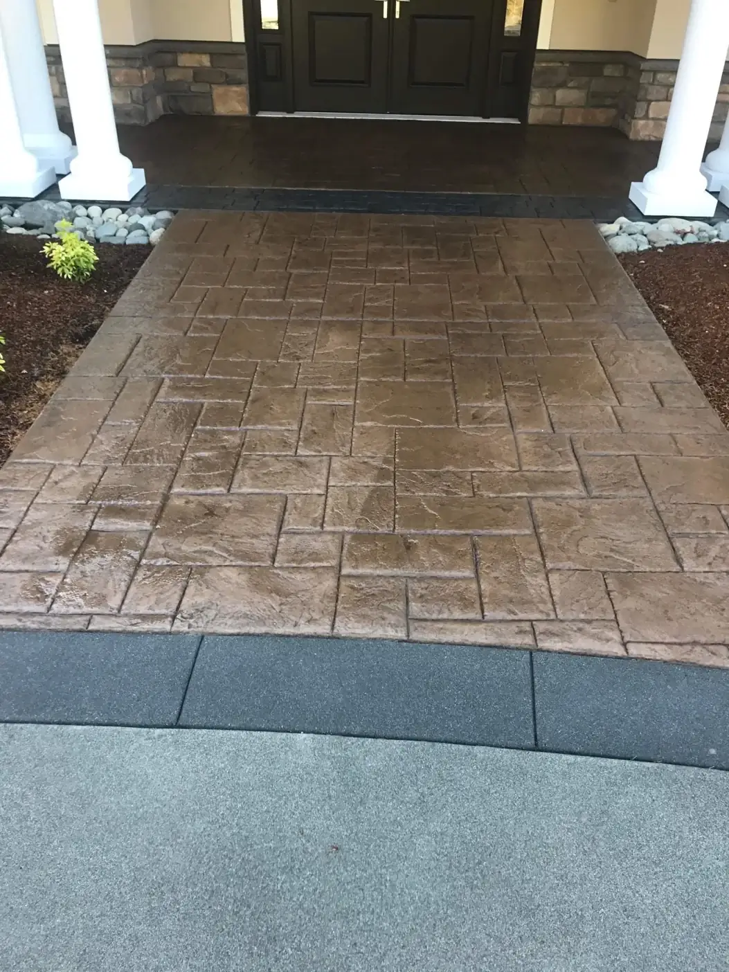 Front-on perspective of the ashlar slate stamped concrete walkway leading to a dark front porch in Tacoma, WA.
