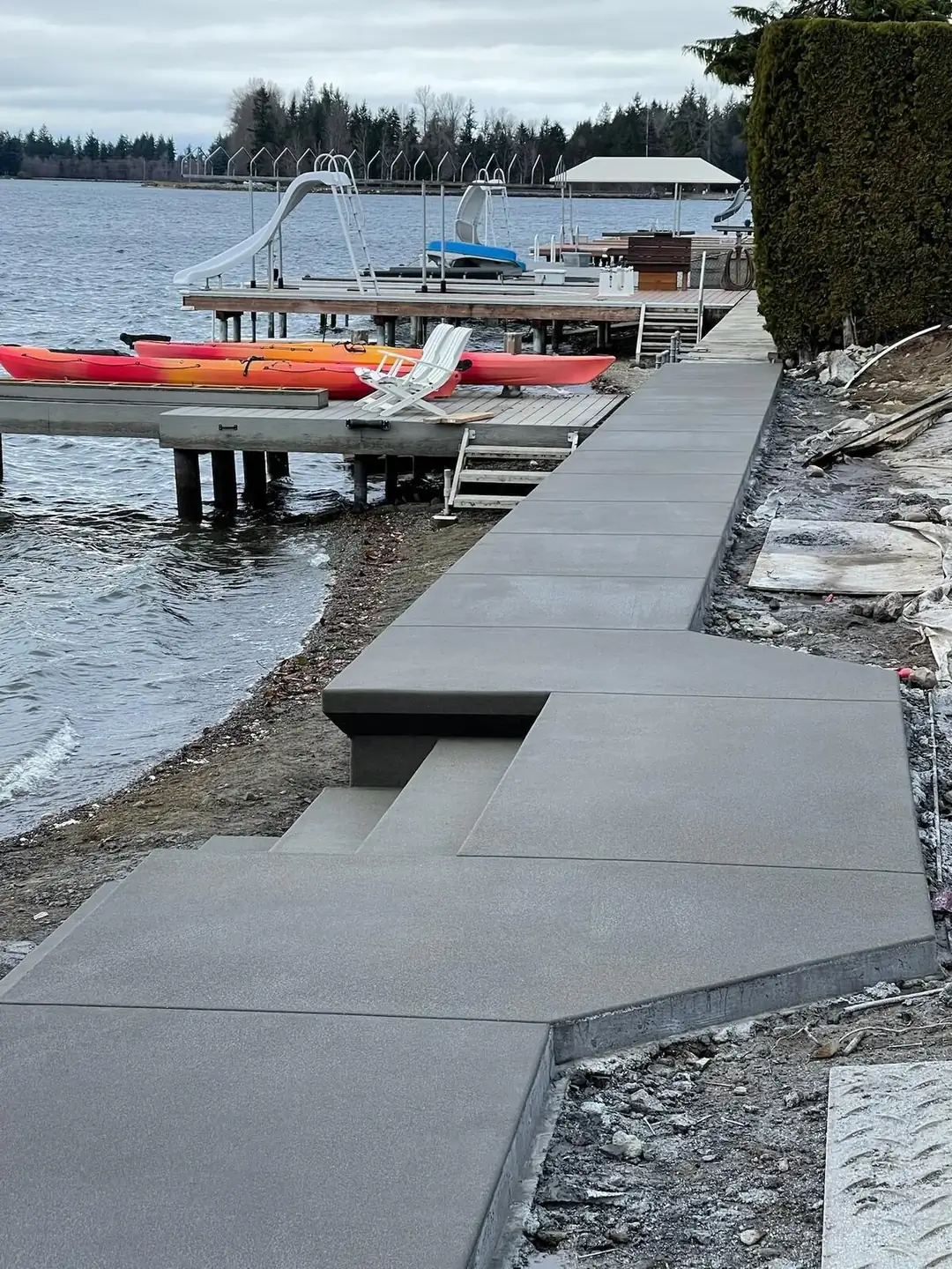 Long concrete walkway with an exposed aggregate finish running along a lake shoreline next to a dock.