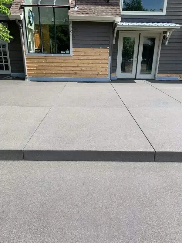 Front view of a new concrete patio with a sand finish and a single step leading to a doorway in Waller, WA.