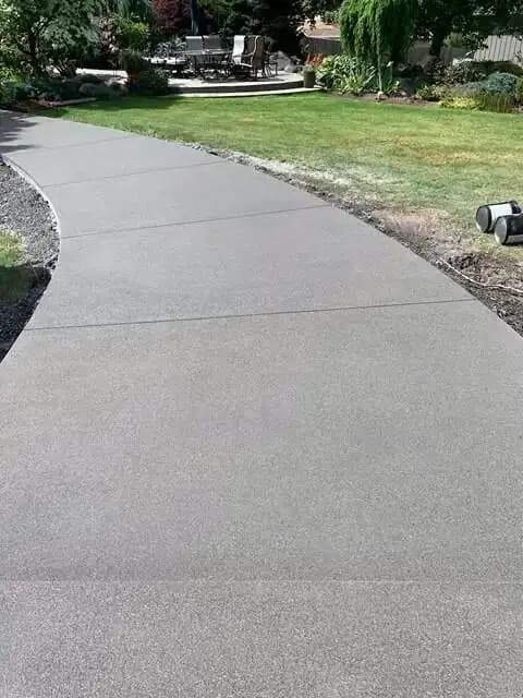 Long view of a curving concrete walkway with a sand finish leading into a lush green backyard.