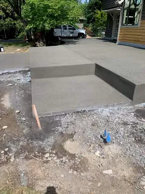 Corner view of a newly poured concrete step and patio foundation with a sand finish in Waller, WA.
