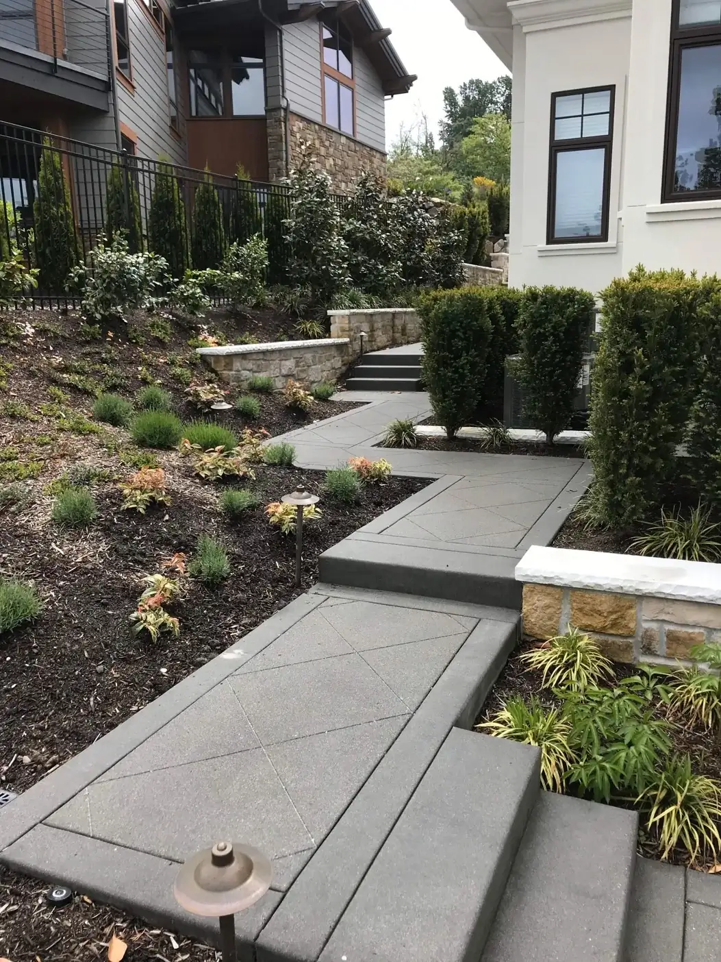 A winding exposed aggregate concrete walkway with integrated steps and saw-cut patterns in a Bellevue home's garden.