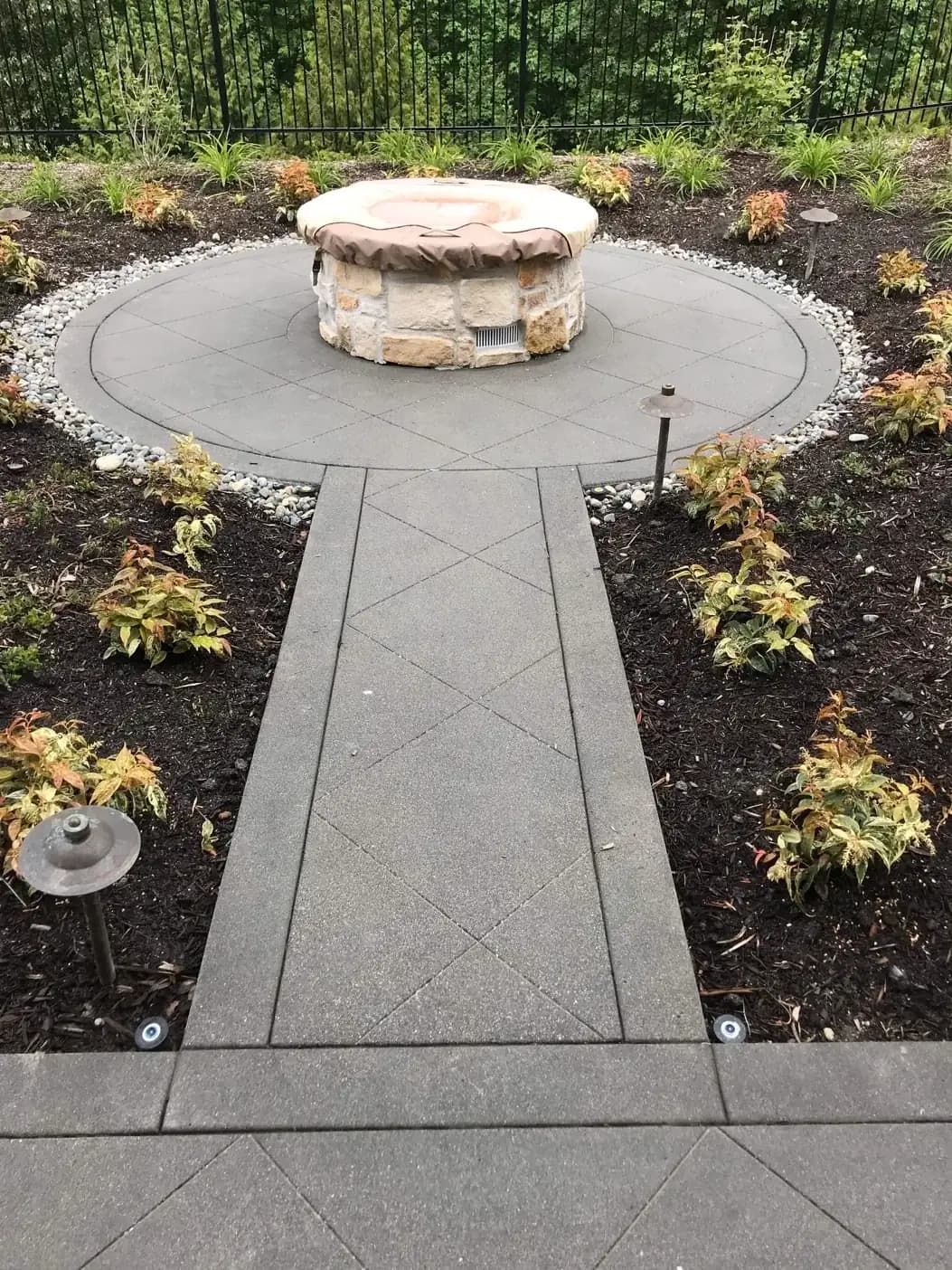 Circular exposed aggregate patio with a stone fire pit and radial saw cuts, part of a Bellevue walkway system.