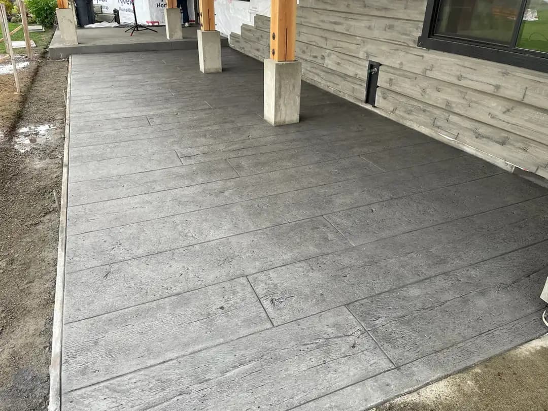 Wide view of a new stamped concrete patio in Puyallup, featuring a realistic gray wood plank pattern and texture.