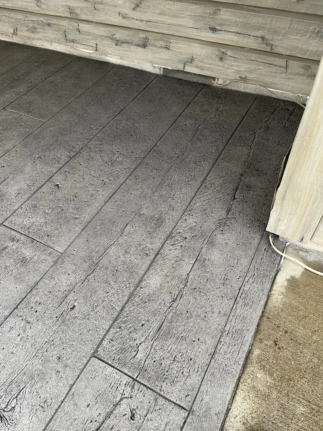 Corner view of a wood-look stamped concrete patio in Puyallup, meeting the home's foundation and siding.