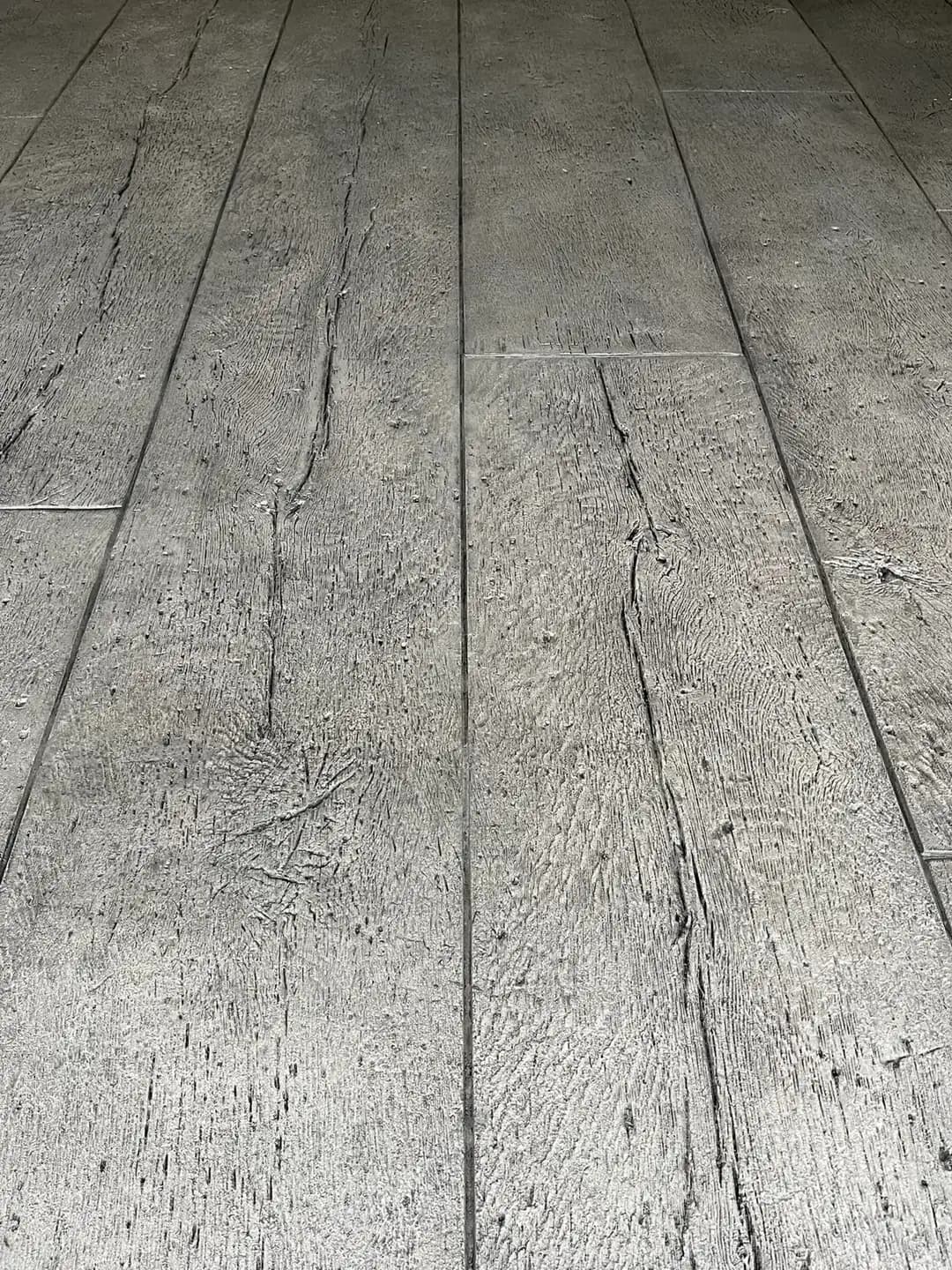 Low-angle perspective of a stamped concrete surface with a detailed, weathered wood grain and knot texture.